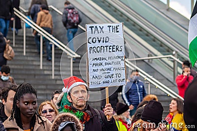 STRATFORD, LONDON, ENGLAND- 5 December 2020: Anti-lockdown Standupx protester holding a â€˜Tax the covid profiteersâ€™ placard Editorial Stock Photo